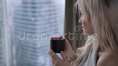 美丽的金发女人拿着陶瓷杯的茶或咖啡享受。 在床上<strong>喝茶</strong>。 看着窗户<strong>喝茶</strong>